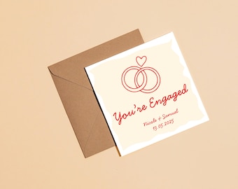 Könnte beinhalten: Eine Verlobungsankündigungskarte mit einem roten Ringdesign und dem Schriftzug "You're Engaged". Die Karte wird von einem braunen Umschlag begleitet, alles vor einem hellbeigen Hintergrund. Die Namen Nicole und Samuel und das Datum 13.05.2025 sind ebenfalls enthalten.