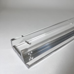 May include: A clear, rectangular acrylic object with a channel running along its length. The object has a series of small, evenly spaced holes. The edges are clean and sharp, reflecting light. The overall design is minimalist and modern.