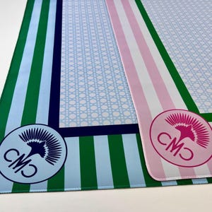 May include: Two decorative mats with striped and patterned designs. One mat features green and light blue stripes with a blue and white logo. The other mat has pink and white stripes with a pink and white logo. Both mats have a light blue patterned center.