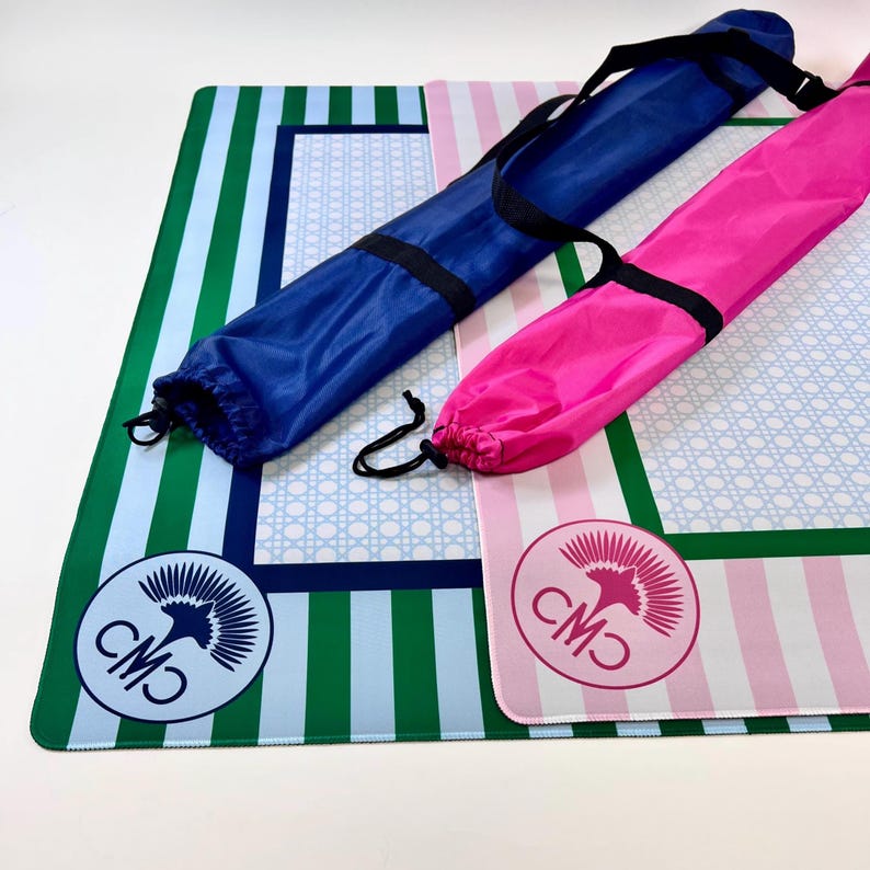 May include: Two colorful beach mats with matching carrying cases. One mat features green and blue stripes, the other pink and white stripes. Both have a circular logo and a blue or pink carrying case.