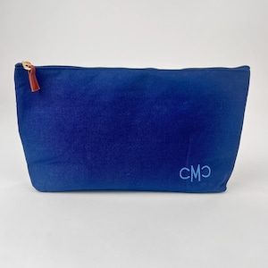 May include: A blue corduroy cosmetic bag with a gold zipper and a brown leather pull. The bag has the embroidered initials "CMO" in a lighter shade of blue.