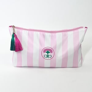 May include: Pink and white striped cosmetic bag with a pink zipper and green and pink tassels. The bag features a circular emblem with the initials "CMO" in green. The bag is designed for storing makeup and other beauty products.