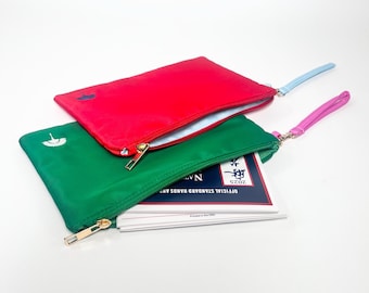 May include: Two zippered pouches, one red and one green, with wrist straps. The red pouch has a blue umbrella logo, and the green pouch has a white umbrella logo. The green pouch is partially unzipped, revealing a stack of cards.