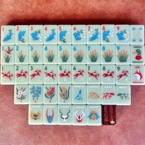 May include: A complete set of Mahjong tiles, featuring various symbols and numbers. The tiles are light green with illustrations of fish, reeds, horses, and dragons. The set includes tiles marked "North", "South", "East", and "West", as well as "Joker" tiles.