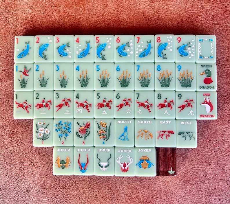 May include: A complete set of Mahjong tiles, featuring various symbols and numbers. The tiles are light green with illustrations of fish, reeds, horses, and dragons. The set includes tiles marked "North", "South", "East", and "West", as well as "Joker" tiles.