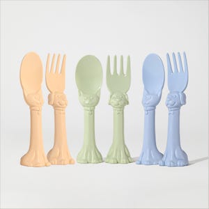 May include: Set of six colorful plastic toddler utensils with animal designs. The set includes two blue spoons and forks, two green spoons and forks, and two orange spoons and forks.