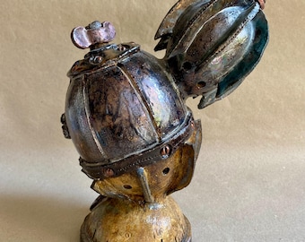 May include: A handcrafted, steampunk-inspired sculpture with a metallic finish. The sculpture features a rounded body, a hinged top, and a detailed base. The color palette includes shades of bronze, copper, and dark brown, creating a vintage aesthetic.