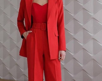 Könnte beinhalten: Ein leuchtend roter Hosenanzug mit Blazer, Oberteil mit herzförmigem Ausschnitt und weiten Hosen. Der Blazer hat ein fallendes Revers und einen Ein-Knopf-Verschluss. Der Hosenanzug ist an der Taille gegürtet. Das Outfit ist einfarbig und kräftig.