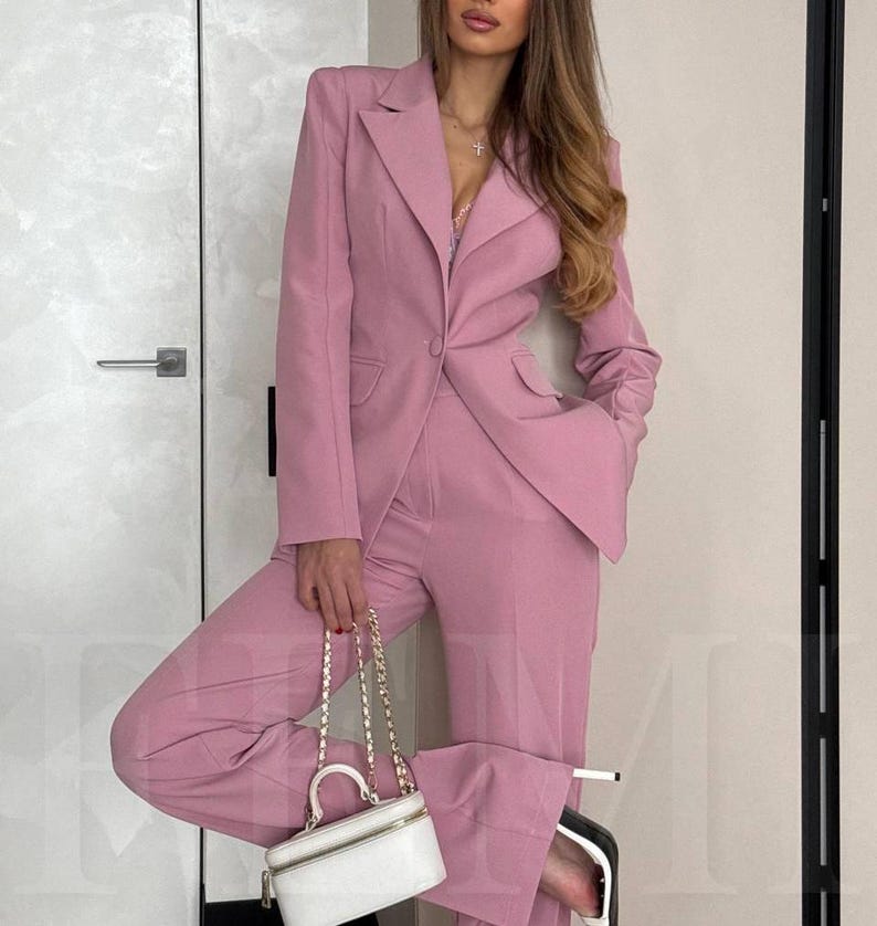 K&ouml;nnte beinhalten: Ein rosafarbener Blazer und eine passende Hose. Der Blazer hat einen Knopfverschluss und einen Schalkragen. Die Hose hat eine weite Beinweite.