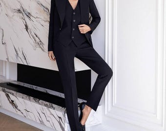 May include: A black three-piece suit consisting of a tailored blazer with notched lapels, a button-front vest, and matching slim-fit trousers. The ensemble is completed with a pair of black pointed-toe high-heeled pumps, creating a formal look.