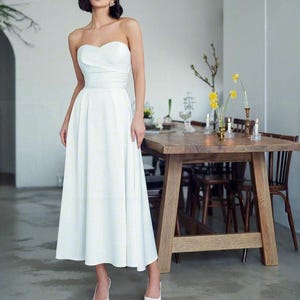 May include: A white strapless dress with a fitted bodice and a flowing skirt. The dress is made of a smooth, satin-like fabric.