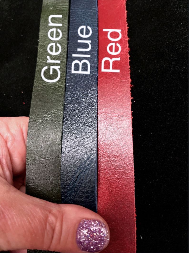 May include: Three leather strips in green, blue, and red are displayed. Each strip has a white label with its respective color name. The leather has a textured surface. The background is black.