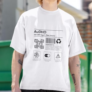 May include: White t-shirt featuring a black graphic design that reads "AUDHD aw-dee-eych-dee (noun)" and includes a QR code, a list of "ingredients", and three icons. The icons are labelled "In need of structure but can't stick to it", "Hyperfocus mode activated", and "Warning: May experience overthinking and anxiety".