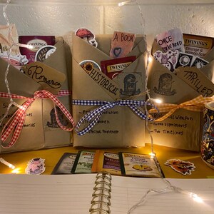 May include: Three brown paper packages wrapped with ribbon and decorated with stickers. Each package is labeled with a genre: "Romance", "Historical", and "Thriller". The packages are sitting on a table with a notebook, tea bags, and a mug.