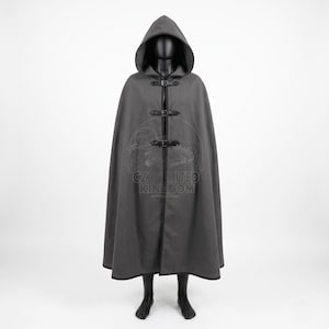 May include: A floor-length charcoal gray hooded cloak featuring three black leather-style straps with metal buckles down the front. The garment has a wide hood and a dark trim along the edges. A faint logo with the text CZY UNITED KINGDOM is visible.