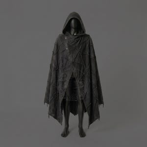 May include: A dark gray hooded cloak with a patchwork design. The cloak features a button closure and a draped front. The garment is displayed on a mannequin against a gray background. The cloak has a distressed, textured appearance.