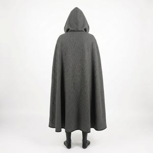 May include: A floor-length charcoal gray hooded cloak featuring a subtle, repeating tonal pattern across the fabric. The garment has a structured hood and a wide, flowing silhouette that extends to the hem, finished with a dark trim along the edge.