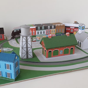 May include: A paper model of a small town with a train track, a water tower, a church, and several houses. The houses are painted in various colors, including red, blue, green, and yellow.