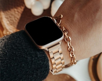 May include: A gold-colored smartwatch with a black screen is worn on a wrist. The watch has a matching gold band and is paired with a gold chain bracelet. The watch and bracelet are set against a dark background.