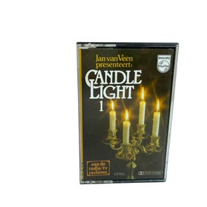 Pode incluir: Uma cassete Philips intitulada Candle Light 1, apresentada por Jan van Veen. A capa apresenta um candelabro dourado com quatro velas brancas acesas contra um fundo escuro, com o texto van de radio/tv reclame e a palavra stereo.