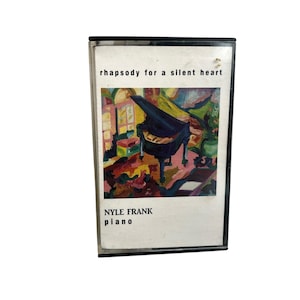 Op de afbeelding: Een vintage cassettebandje met een kleurrijk abstract schilderij van een vleugel. Het label van de tape luidt "rhapsody for a silent heart" en "NYLE FRANK piano". Het kunstwerk toont levendige tinten blauw, geel, rood en groen.