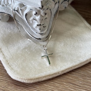 May include: A silver-toned necklace featuring a simple, polished cross pendant suspended from a delicate box chain. The cross has clean, straight lines and a smooth, reflective surface, showcasing a classic design that hangs from a small jump ring.