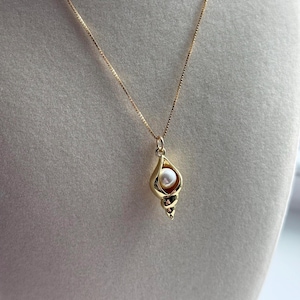 May include: A gold chain necklace with a pendant shaped like a seashell with a pearl inside.