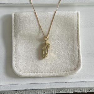 May include: A gold-colored necklace with a pendant shaped like a sneaker. The pendant is detailed with small, clear stones. The necklace is displayed on a white, rectangular, fabric-lined tray.