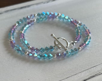 May include: A delicate double-strand bracelet featuring iridescent blue and purple crystal beads with a silver toggle clasp.