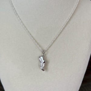 May include: A silver necklace featuring a pendant shaped like a running shoe. The pendant is detailed with small, sparkling stones. The chain is a delicate, twisted design, and the necklace is displayed on a neutral background.