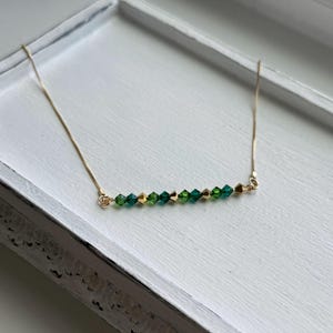 May include: A delicate gold chain necklace with a row of green and gold crystal beads.