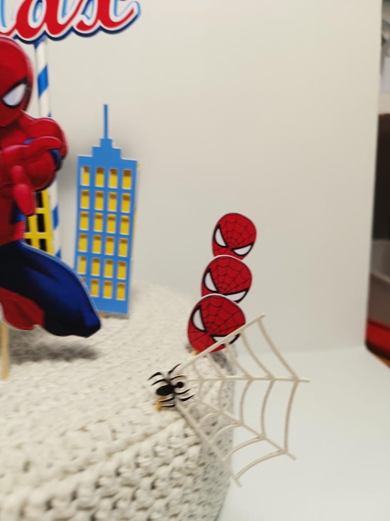 Puede incluir: Un juego de adornos para tartas con tem&aacute;tica de Spiderman. Incluye una figura de Spiderman, un rascacielos azul y recortes de m&aacute;scaras de Spiderman. Tambi&eacute;n se incluye una telara&ntilde;a blanca y una peque&ntilde;a ara&ntilde;a negra.