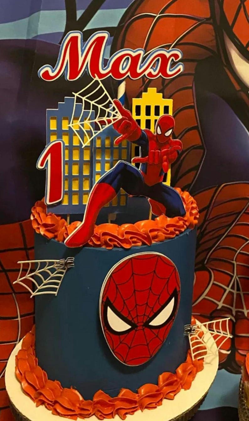 Puede incluir: Una tarta azul decorada con la tem&aacute;tica de Spider-Man. La tarta presenta una figura de Spider-Man, un paisaje urbano y el nombre "Max" en rojo. Tambi&eacute;n se muestra el n&uacute;mero "1", lo que indica una celebraci&oacute;n de primer cumplea&ntilde;os. La tarta est&aacute; adornada con crema de mantequilla naranja.