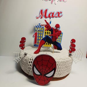 Puede incluir: Adorno para tarta con una figura de Spider-Man rojo y azul, un edificio y el nombre "Max" con el n&uacute;mero "1". El adorno incluye telara&ntilde;as y detalles de ara&ntilde;as, ideal para una celebraci&oacute;n de cumplea&ntilde;os.