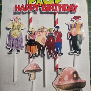 Op de afbeelding: Taarttoppers met de tekst "PLOP HAPPY BIRTHDAY" en stripfiguren. De toppers bevatten afbeeldingen van stripfiguren, een paddenstoel en een paddenstoelenhuis. De toppers zijn bevestigd aan witte stokjes met rood-witte strepen.