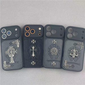 Pode incluir: Quatro capas pretas para smartphone com painéis traseiros de textura semelhante a couro, adornadas com emblemas metálicos prateados, incluindo cruzes, flores-de-lis e motivos circulares. Cada capa possui uma abertura para as lentes da câmara.