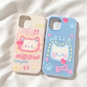 May include: Two rectangular phone cases with rounded corners. The left case is translucent with a pink cat face, the text "yes" and "MEOW", and yellow star and smiley face icons. The right case is light blue with a white cat face, the text "HELLO", a pink heart, a pink bone, and light blue paw prints.