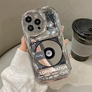 May include: A clear, wavy-edged phone case featuring a central graphic of a compact disc. The design includes black and white stickers, the text "LUCKY- HAPPY", "CLORYCREATION", and "Lucky" printed on the surface, with a cutout for the camera lens.