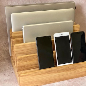 May include: A wooden desk organizer with multiple slots for electronic devices. The organizer holds a laptop, tablet, and three smartphones. The wood has a natural grain and a warm, light brown color.