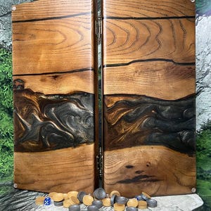 Puede incluir: Juego de backgammon con exterior de madera y un diseño de resina epoxi oscura y arremolinada. El juego está abierto, revelando la superficie de juego, e incluye una colección de fichas y dados.