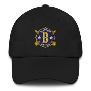 May include: Black baseball cap featuring an embroidered emblem. The emblem displays the words "Boston Blues" around a large letter "B" and two crossed baseball bats. Two stars flank the letter "B".