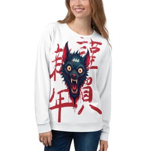 Peut inclure: Sweat-shirt blanc à manches longues avec un motif noir et rouge d'un loup qui grogne avec le nombre 666 sur son front. Le loup est entouré de caractères japonais rouges.