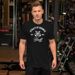 Op de afbeelding: Zwart T-shirt met een witte opdruk met de tekst "STRAIT OF HORMUZ" boven een anker en scheepsrad ontwerp. Onder de afbeelding staat de tekst "Yacht Club". Het shirt heeft ook de tekst "EST. 1979".