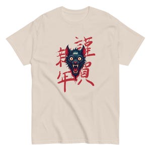 Peut inclure: Un t-shirt beige avec un motif noir et rouge d'un loup qui grogne avec le nombre 666 sur son front. Le loup est entouré de caractères japonais rouges.