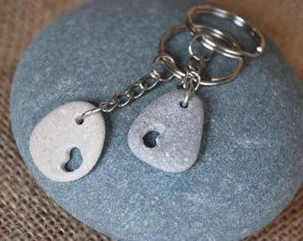 Könnte beinhalten: Ein Set aus zwei grauen und weißen Stein-Schlüsselanhängern mit Herz-Ausschnitten, befestigt an einer silbernen Kette und einem Schlüsselring.
