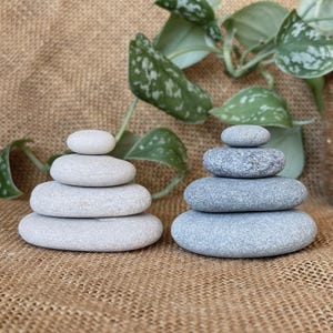 Puede incluir: Se muestran dos conjuntos de piedras apiladas, uno en gris claro y otro en gris más oscuro. Las piedras tienen forma ovalada y están dispuestas en un diseño equilibrado y en capas. El texto "Set 1" es visible en la esquina superior izquierda.