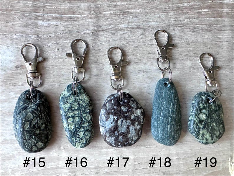 K&ouml;nnte beinhalten: F&uuml;nf Schl&uuml;sselanh&auml;nger mit Natursteinen in einzigartigen Texturen und Farben, jeweils an einem silberfarbenen Metallkarabiner befestigt. Die Steine sind mit #15, #16, #17, #18 und #19 beschriftet und zeigen verschiedene Gr&uuml;n-, Braun- und Graut&ouml;ne.
