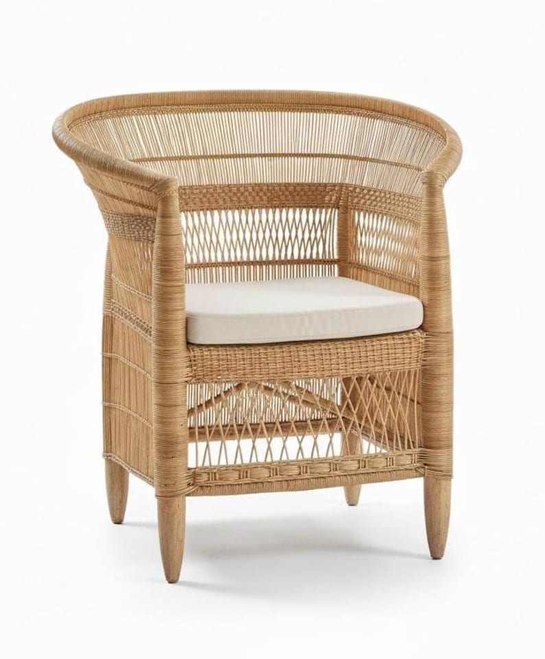 May include: A natural wicker armchair with a curved back and armrests. The chair features a woven design and a cream-colored cushion. The legs are made of wood. This chair is suitable for indoor or outdoor use.