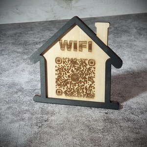 Peut inclure: Panneau en bois en forme de maison avec le mot « WIFI » et un code QR gravés. Le cadre est gris foncé et l'intérieur est en bois naturel. Un objet décoratif pour afficher les détails du réseau WiFi.