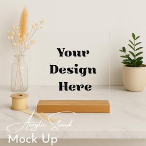 Puede incluir: Soporte de acrílico transparente con base de madera. El texto "Your Design Here" se muestra en negro. Las palabras "Acrylic Stand Mock Up" están escritas en una fuente cursiva. Un jarrón con flores secas y una pequeña planta en maceta están en el fondo.
